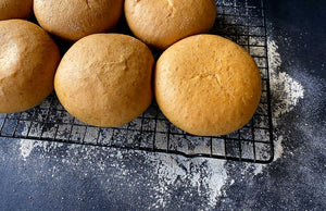 Bread buns on a baking rack on a flour-dusted table